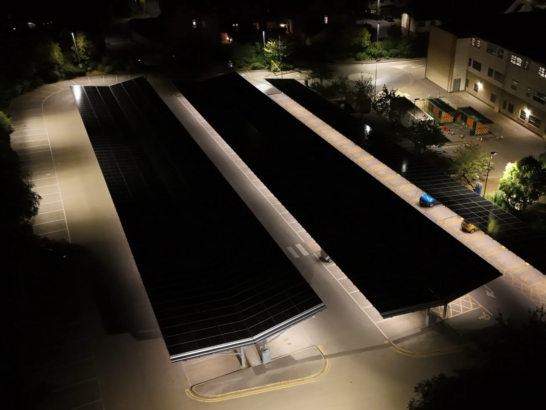 Night drone aerial of Wharfedale Hospital car park illuminated beneath Bluetop Solar OPTI solar canopies generating clean energy